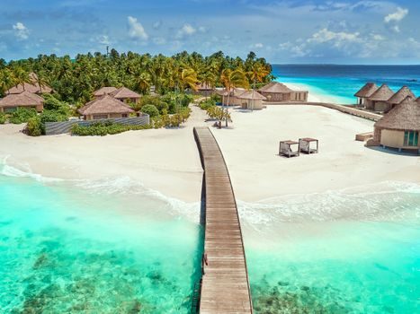 rangée de chalets en bois sur pilotis face à une plage de sable blanc, végétation tropicale dense en arrière-plan, ciel dégagé en fin de journée