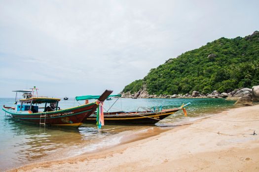 longue-tail boat en bois amarrée devant un îlot tropical densément boisé, jungle qui descend jusqu'au sable, lumière de fin d'après-midi